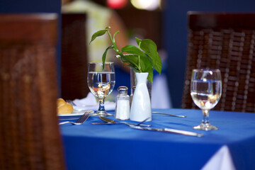 Glass glasses with water on the dining table, along with Cutlery and a flower in a vase, standing on a blue tablecloth.