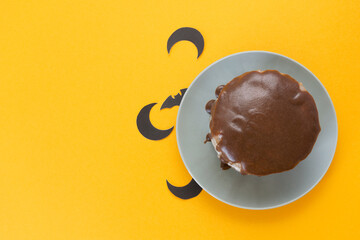 Bat and moon under a plate. Chocolate cake on orange background. Halloween concept, trick or treat. Handmade cooking. Copy space, flat lay. Selective focus, blur.