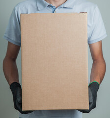 Detail of man with black gloves holding a cardboard box for delivering products on gray background. Delivery concept. Delivery service concept. Copy space.