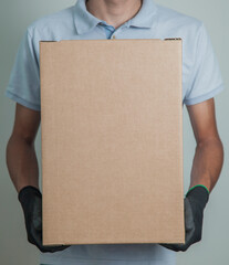 Detail of man with black gloves holding a cardboard box for delivering products on gray background. Delivery concept. Delivery service concept. Copy space.