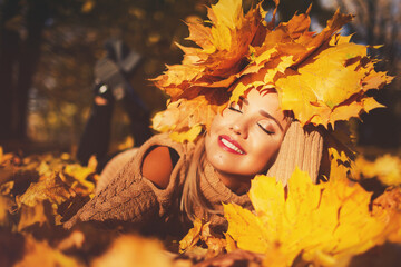 Naklejka na ściany i meble Outdoors lifestyle close up portrait of stunning young woman lying on the grass. Wearing a wreath of autumn leaves. Smiling, walking on the autumn park. Wreath of maple leaves. Autumn colors. Happy