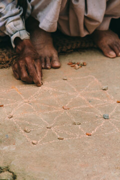Man playing board game drawn on the ground with pebbles