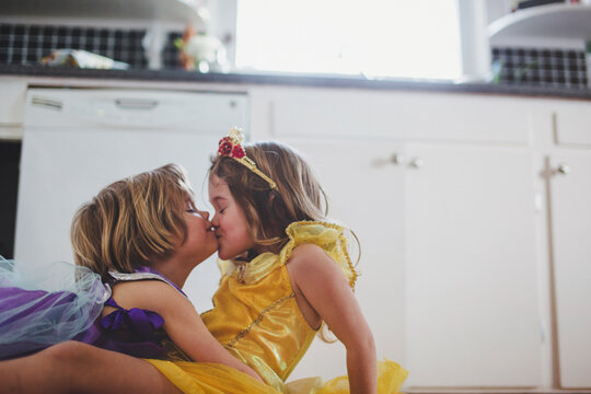 Two preschool-aged sisters kissing in princess dresses