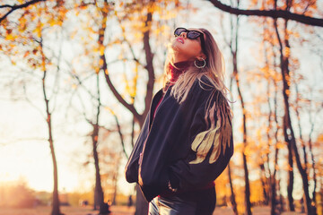 Outdoors lifestyle fashion portrait of beautiful trendy young woman walking on the autumn park. Wearing stylish bomber jacket, sunglasses and leather leggins. Enjoying autumn nature.  
Looking up