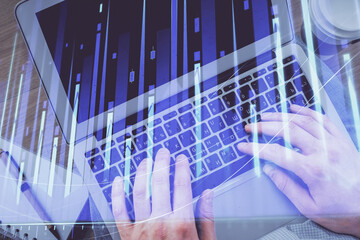 Double exposure of man's hands typing over computer keyboard and forex graph hologram drawing. Top view. Financial markets concept.