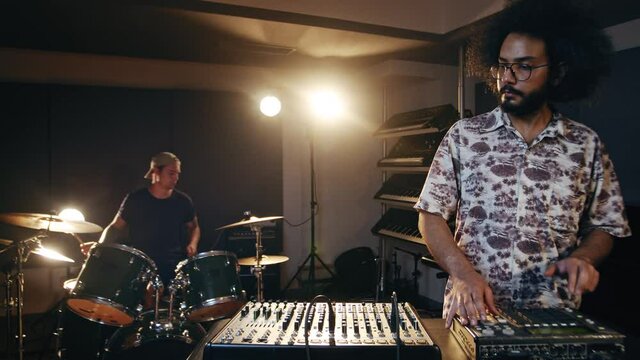Music concept. Band rehearsal. Caucasian man playing drums, hispanic man doing beatmaking. Talented musicians record their ideas.