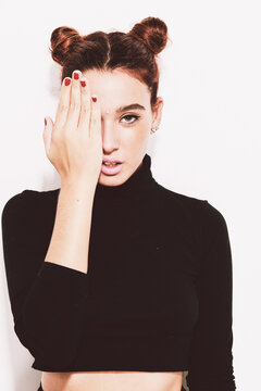 Pretty girl with buns and piercings covering eye with hand.