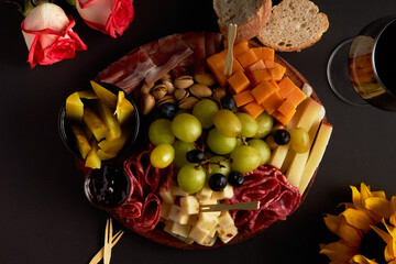 Wooden board with different types of cheese, cold meats, bread and wine