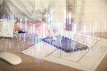 Double exposure of man's hands holding and using a digital device and forex graph drawing. Financial market concept.