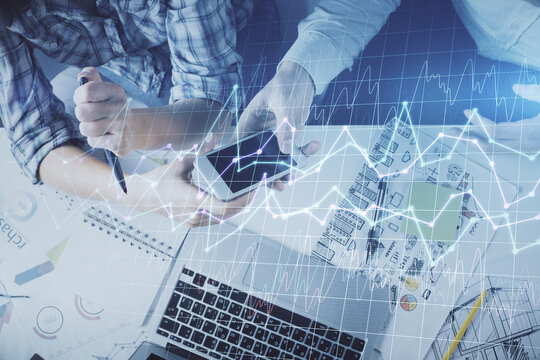 Double exposure of forex graph drawing and man and woman working together holding and using a mobile device. Trade concept.