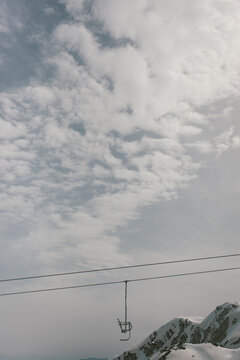 A single seat chairlift with some snowy mountains in the background.
