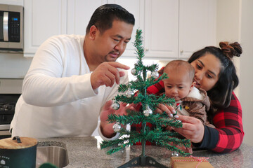 Loving Filipino and Mexican Interracial Parents Celebrate The Holidays Together By Decorating A Tree With Their Mixed Baby Wearing A Reindeer Onesie 