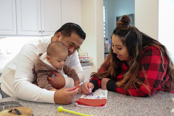 Loving Filipino and Mexican Interracial Couple Celebrate The Holidays Together By Decorating Holiday Stocking With Their Mixed Baby Wearing A Reindeer Onesie 