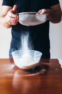 Man sieves flour into a glass bowl