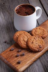 White cup of cocoa, oatmeal cookies with chocolate on old wooden background