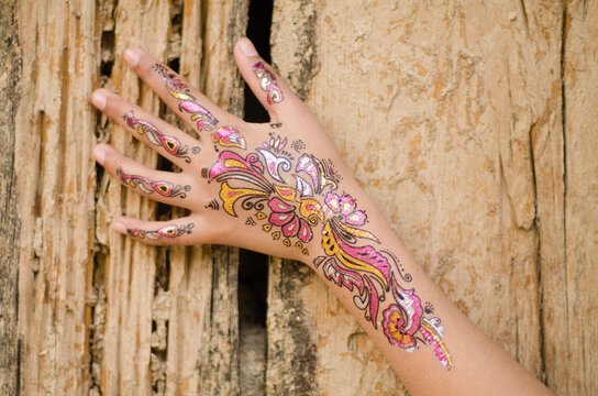A henna tattoed hand of an adolesecnce girl placed over a wooden wall