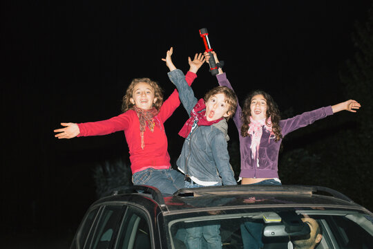 3 extremely excited children waving their hands and partying while staying on top of the car