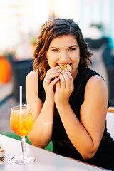 Happy young woman having foccacia snack and iced aperol spritz cocktail after work