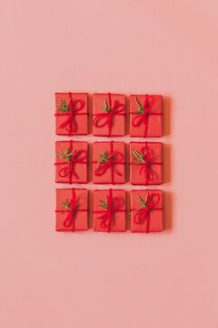 Small red christmas gifts with rosemary decoration in a grid on pink