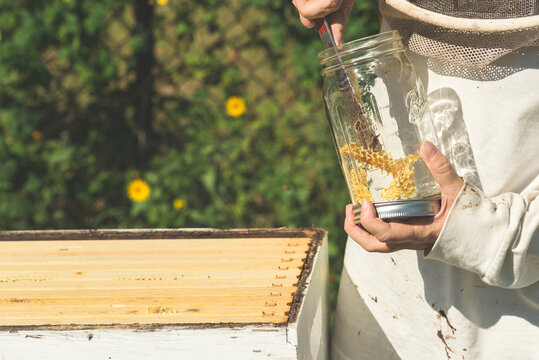 A Female Beekeper Putting Extra Honeycomb In A Glass Jar