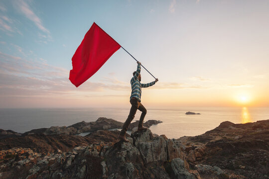 Man waving a red flag in a cliff.