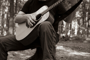 Fototapeta na wymiar Monochrome. The man plays the guitar. Guitar and hand close- up. Forest background.