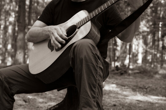 Monochrome. The man plays the guitar. Guitar and hand close- up. Forest background.