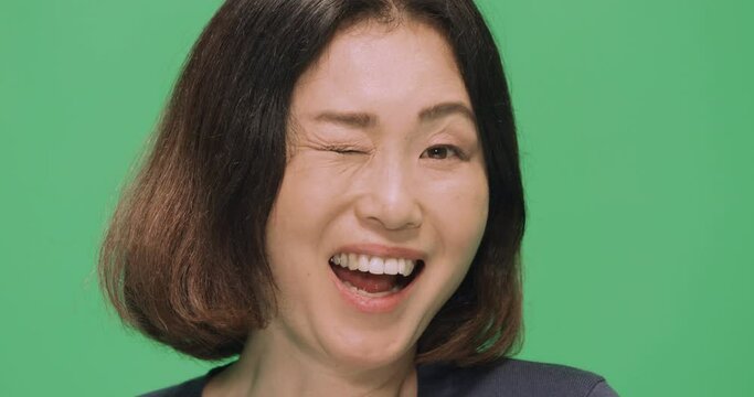 Studio, slow motion, a portrait of a Japanese woman winking against a green screen, London, UK