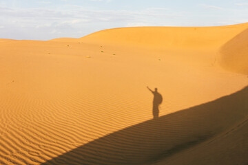 Shadow of a young victorious man on a dune on the desert