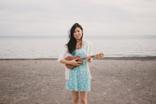 Attractive young asian woman playing the ukelele on the beach
