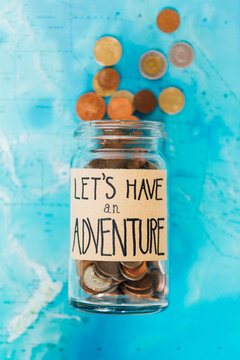 Money jar with coins on atlas labelled ""Let's Have An Adventure""