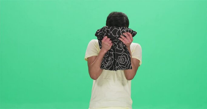 Young Chinese man crying and hiding behind cushion, green screen