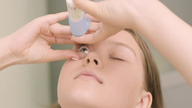 The young girl instill eye drops before installing Night time Contact Lenses in an ophthalmologist's office. Eyedropper putting liquid into open eye. Child's eye drops.
