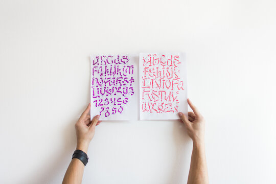 Man hands holding A4 paper with calligraphy designs on clean white wall