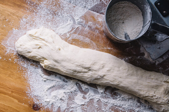Shaped French baguette dough and flour sifter on a wooden table from above