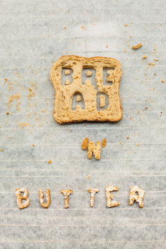 Slice of bread with letters cut out of it and butter written with letters made of bread and butter