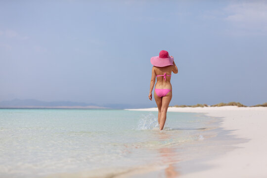 Young anonymous woman in pink bikini and sunhat on idyllic beach
