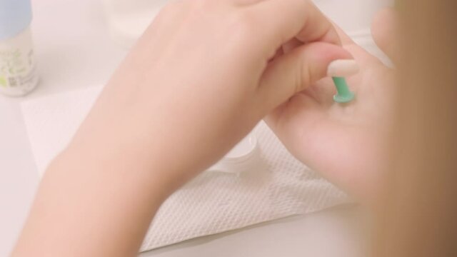 The young girl instill eye drops before installing Night time Contact Lenses in an ophthalmologist's office. Bottle with lens solution and case with contact lenses on table.