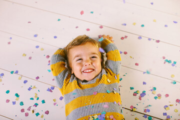Overhead of a happy little boy playing with confetti on white.