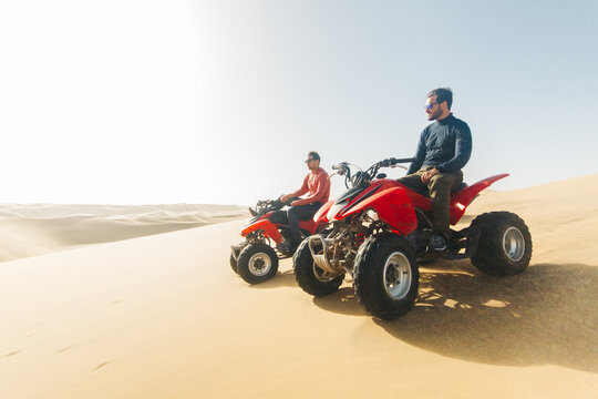 Two young adventurer men on an ATV in the desert overlooking the sand dunes