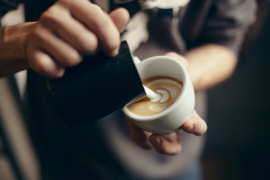 Close up of a barista preparing a coffee milk with flower pattern