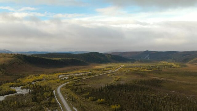 View of Scenic Winding Road surrounded by River, Mountains and Valley in Autumn on a Cloudy Day. Aerial Drone Shot. Taken near Dempster Highway, Yukon, Canada. 4K