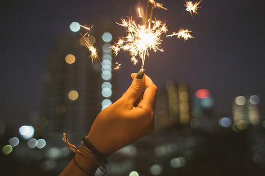 Woman's hand holding a sparkle stick during the night time in the city