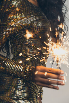 Black woman in golden dress dancing with a sparkler in her hand
