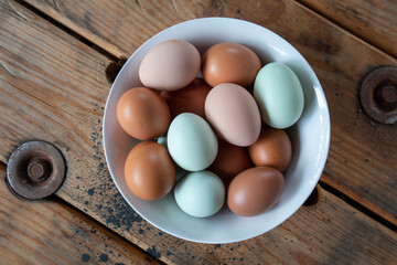 Colorful Fresh Eggs in a white bowl on a wood table - overhead