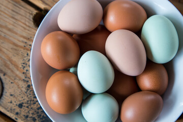 Colorful Fresh Eggs in a white bowl on a wood table - overhead