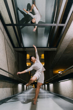 An Asian dancer lifts himself up towards his reflection inside a corridor