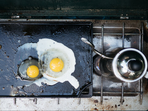 Two eggs frying on cast iron griddle with coffee pot
