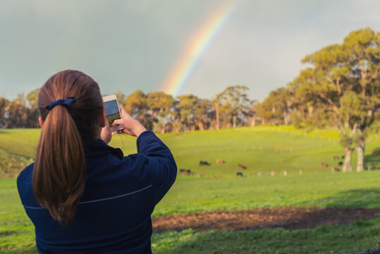 teen girl photographing a double rainbow over a rural farm