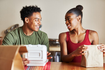 african american couple sitting at table looking at food delivery